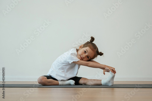 Stretching the leg. Cute little girl is sitting on the yoga mat and doing exercises © standret