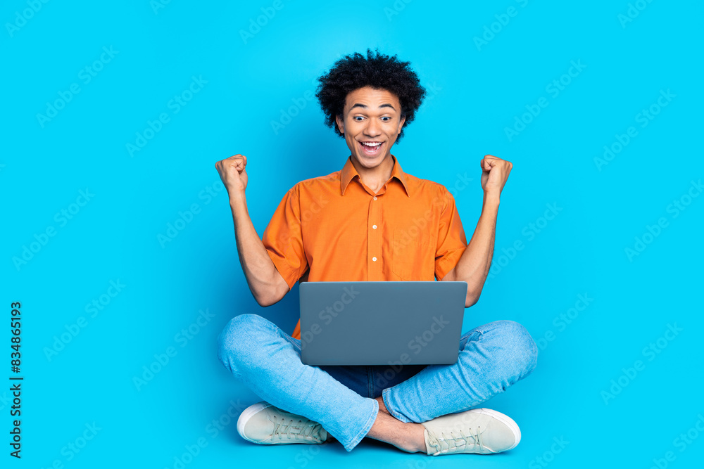 Full length photo of lucky funny guy wear orange shirt winning game modern gadget emtpy space isolated blue color background Full length photo of lucky funny guy wear orange shirt winning game modern gadget emtpy space isolated blue color background