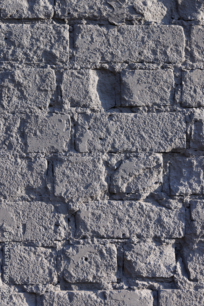 Fototapeta premium The old chipped brick wall is evenly painted over with gray paint. Close-up.