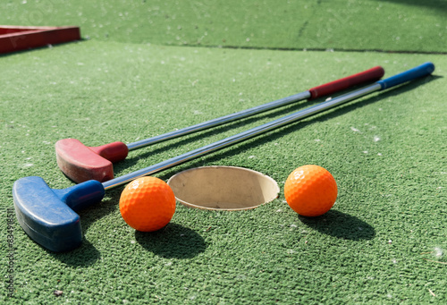 Mini-golf clubs and balls of different colors laid on artificial grass. photo