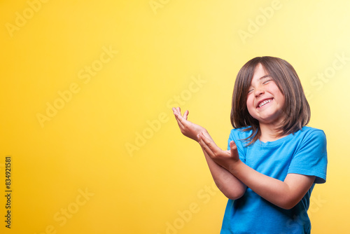 Smiling boy showing space for text and logos. Blue t-shirt. Yellow background. © Oriol Roca