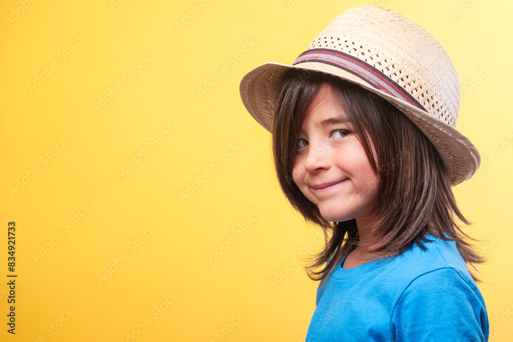 Close-up of smiling child. Blue t-shirt and straw hat. Yellow background. Copy space Close-up of smiling child. Blue t-shirt and straw hat. Yellow background. Copy space
