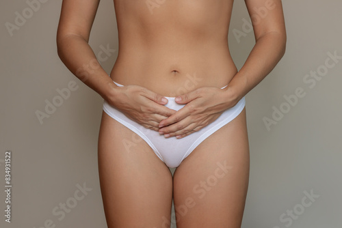 Cropped shot of a young woman in white underwear holding her lower abdomen with hands suffering from painful periods on dark background. Gynecological problems, genital tract infections, inflammation
