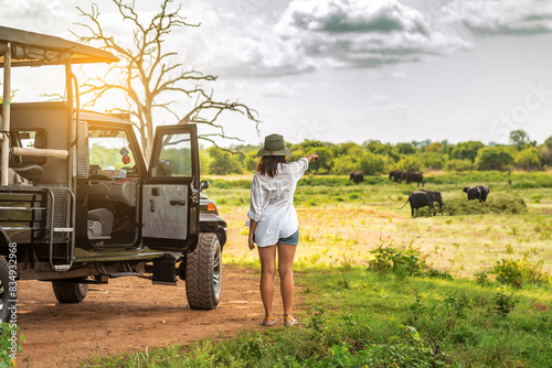 Tourist woman near off road car watching on elephants on safari tour