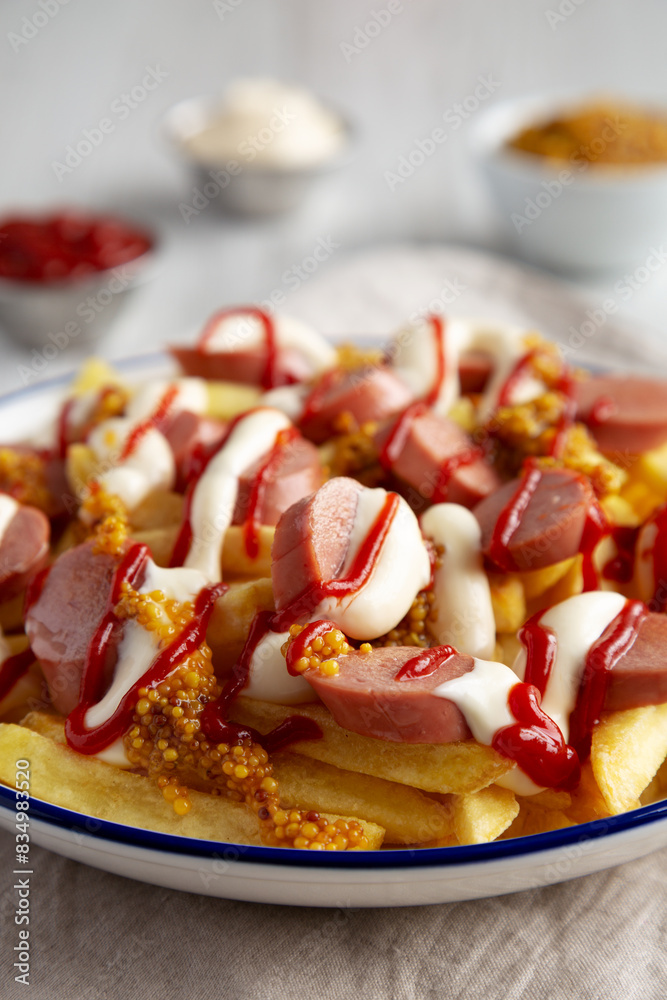 Homemade Salchipapa Fries with Ketchup, Mustard and Mayo on a Plate, low angle view. Close-up. Homemade Salchipapa Fries with Ketchup, Mustard and Mayo on a Plate, low angle view. Close-up.