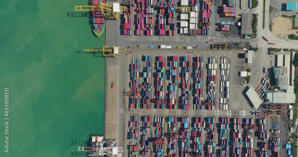 commercial port loading and unloading cargo from container ship import and export by crane for distributing goods by trailers transported to customers and dealers, aerial top down view 4k video