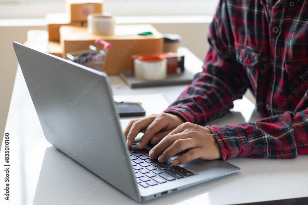 Fototapeta premium businessman decides invest in small SME business at home by using laptop and smartphone do online marketing and sell things online through an application before packing products according to orders.