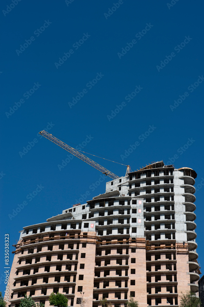 Fototapeta premium Construction of a multi-storey residential building with a crane on a background of blue sky