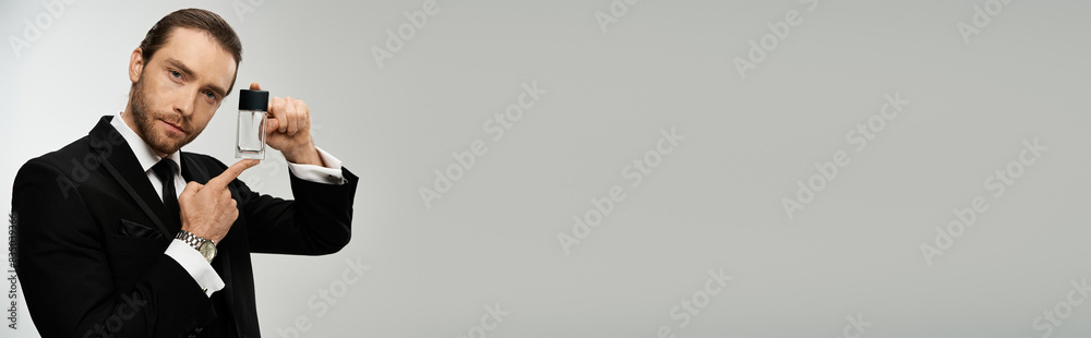 Well-dressed bearded businessman holding bottle with perfume against a grey backdrop. Well-dressed bearded businessman holding bottle with perfume against a grey backdrop.