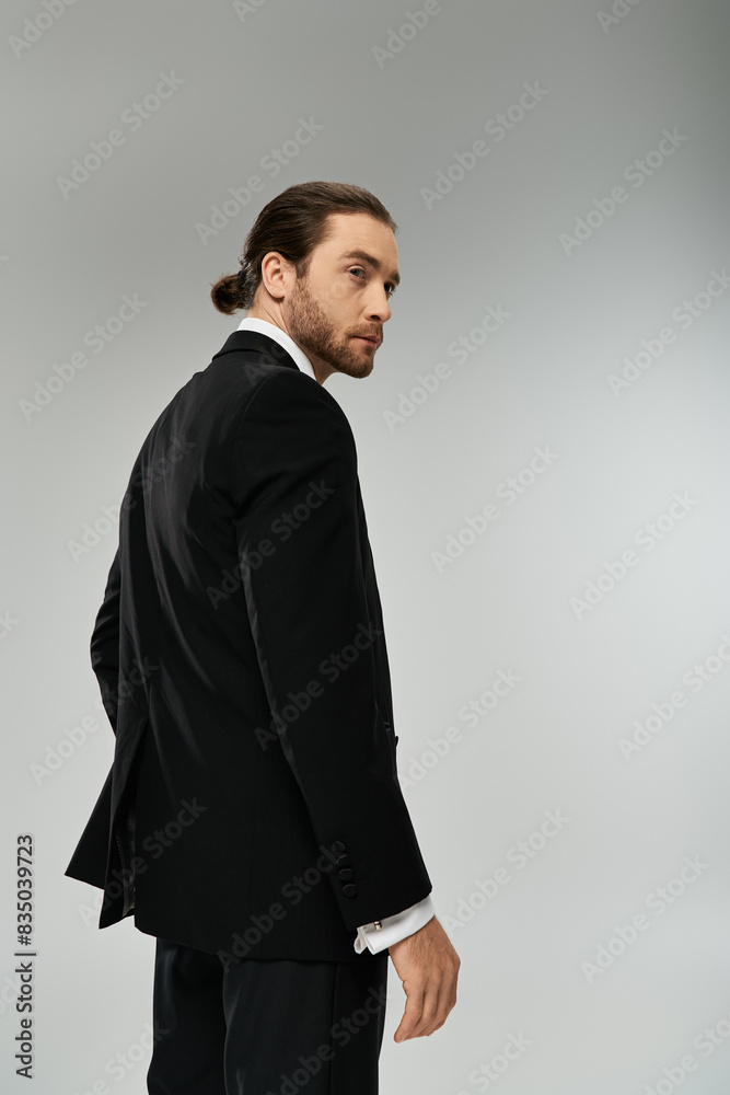 A stylish bearded businessman in a suit confidently stands against a gray background in a studio setting. A stylish bearded businessman in a suit confidently stands against a gray background in a studio setting.