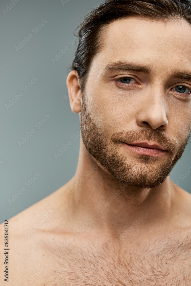 Handsome shirtless man with a beard striking a pose on a grey background in a studio setting. Handsome shirtless man with a beard striking a pose on a grey background in a studio setting.
