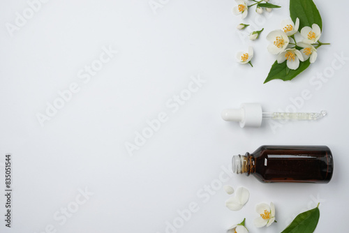 Aroma oil bottle arranged with jasmine flowers on a white background. Flower essential oil. Herbs have medicinal properties. Top view, flat lay. Space for text.