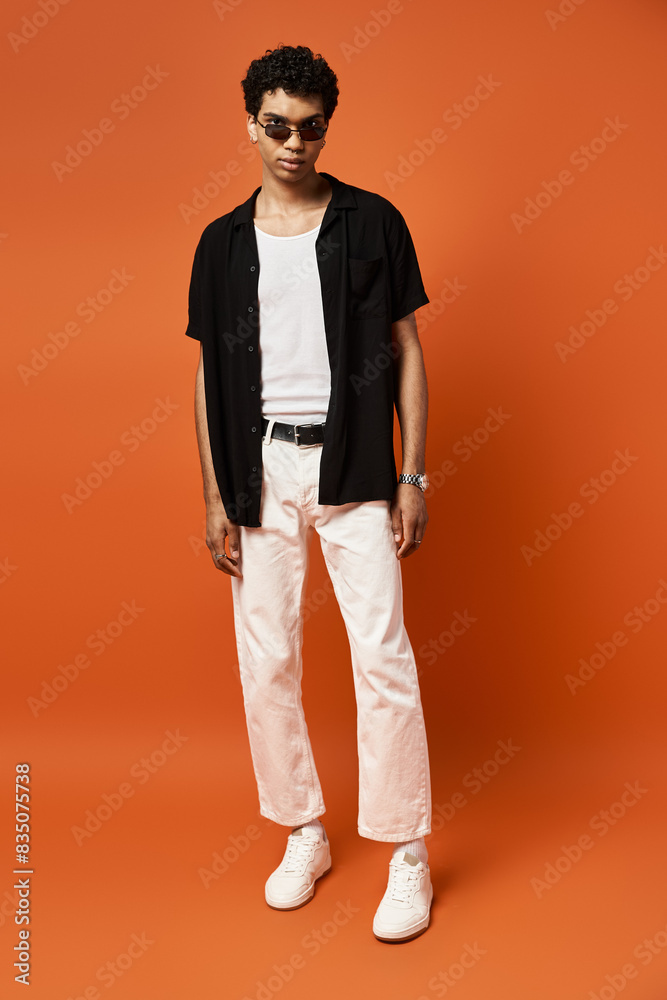 African American man in white pants and black shirt stands against bold orange backdrop. African American man in white pants and black shirt stands against bold orange backdrop.