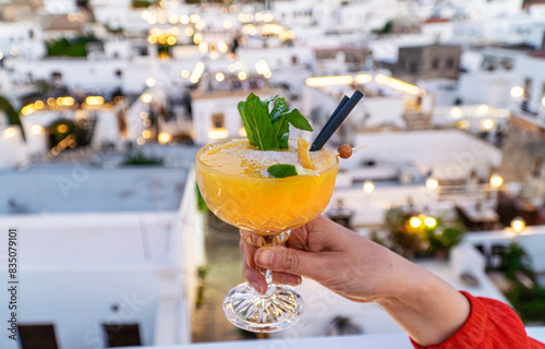 Tableau sur toile A girl holds an orange cocktail against the background of the city