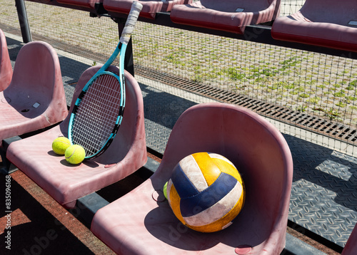 a tennis racket, balls and a volleyball on a bench on the sports tribune