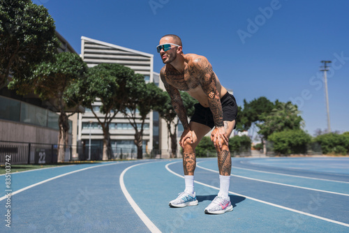 Chico joven musculoso y tatuado en pista de atletismo posando con ropa deportiva photo