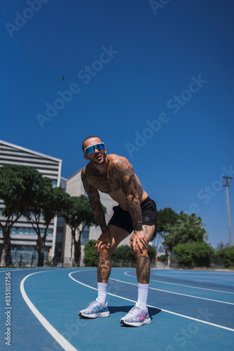 Chico joven musculoso y tatuado en pista de atletismo posando con ropa deportiva