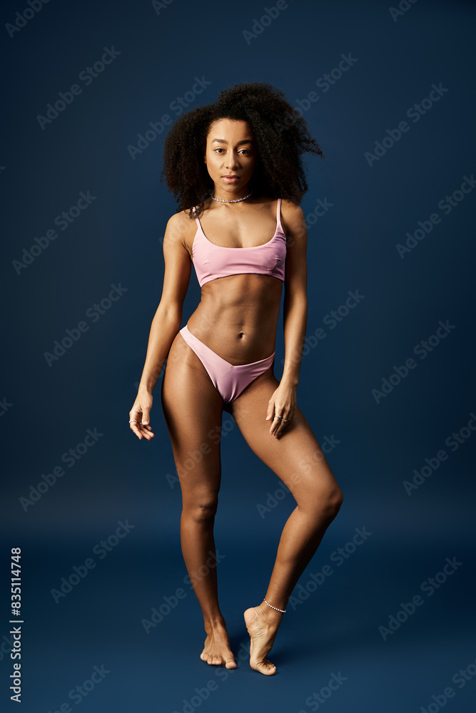 Stylish African American woman striking a pose in a pink bikini against a vibrant blue backdrop. Stylish African American woman striking a pose in a pink bikini against a vibrant blue backdrop.