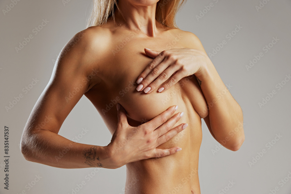 Cropped photo of fit woman poses naked covering her chest with one hand against grey studio background. Concept of beauty and fashion, female health, anti-cellulite, dieting. Ad Cropped photo of fit woman poses naked covering her chest with one hand against grey studio background. Concept of beauty and fashion, female health, anti-cellulite, dieting. Ad