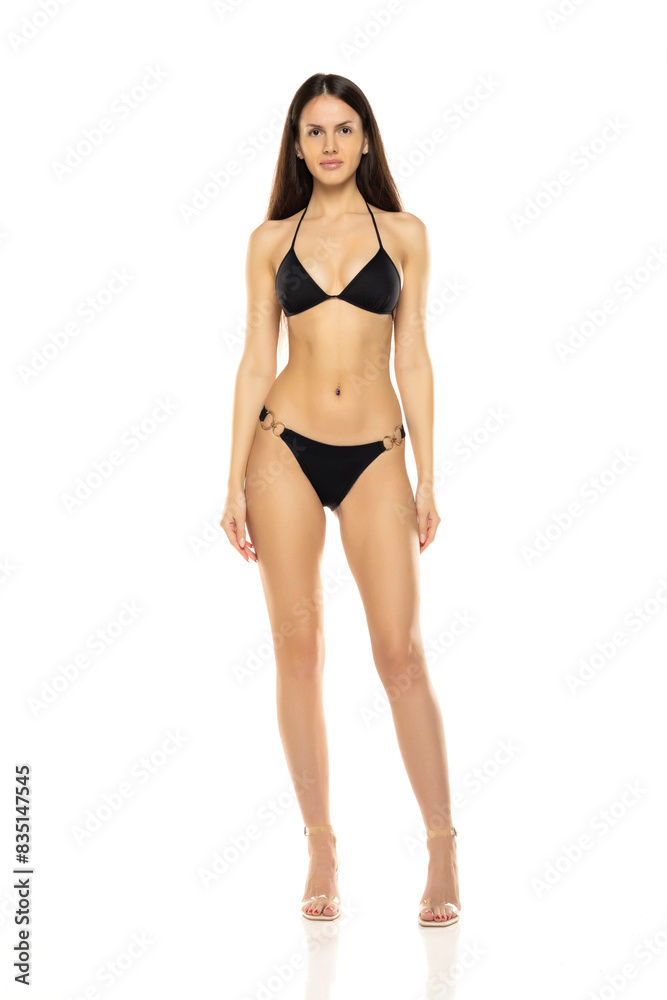 Young brunette woman in bikini swimsuit posing on a white studio background. Front view Young brunette woman in bikini swimsuit posing on a white studio background. Front view