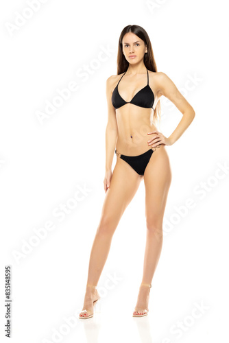 Young brunette woman in bikini swimsuit posing on a white studio background. Front view