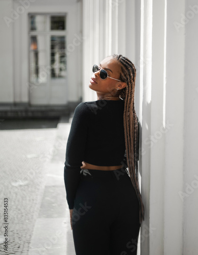 A beautiful young african woman against a white wall, wearing a black long-sleeved top © Alona