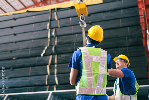 Two young caucasian worker inspects belt for lifting heavy loads on crane hoist in steel factory.