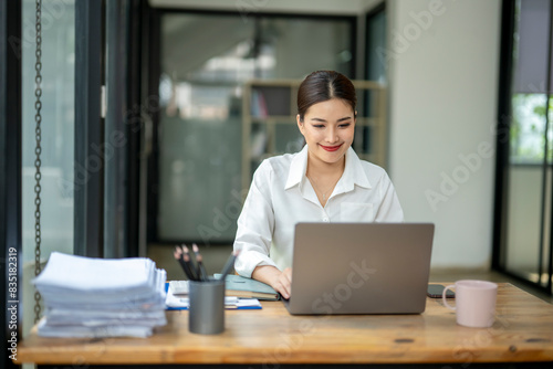 A woman is sitting at a desk with a laptop and a stack of papers