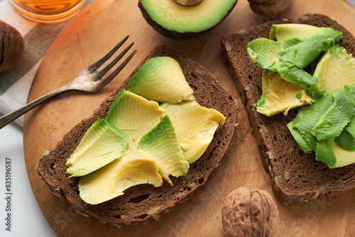 Two slices of whole grain bread topped with avocado, served with a whole walnut on a wooden cutting board.