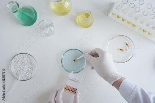 A chemist scientist tests the acidity of a liquid in a petri dish using litmus paper in a laboratory. photo