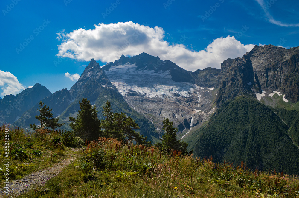 Majestic peaks and mountain valley, Western Caucasus, Dombai. Mountains covered with snow and glaciers. Alpine meadow in the foreground.