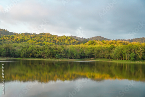 Beautiful nature lake and forest , Jet Khot Nature Study Centre lake and forest in Thailand. Beautiful view of a golden sun shining over a reflective lake under a cloudy sky after sunrise