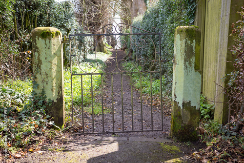 Vintage wrought iron gate leading to mossy path with lush greenery and weathered stone pillars