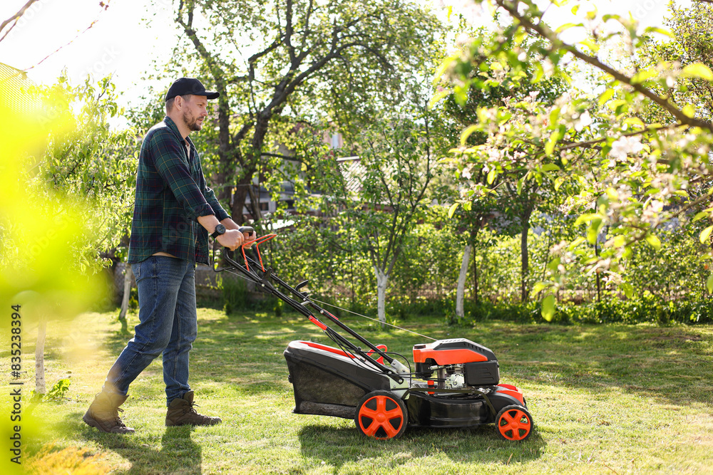 Fototapeta premium Man cutting green grass with lawn mower in garden