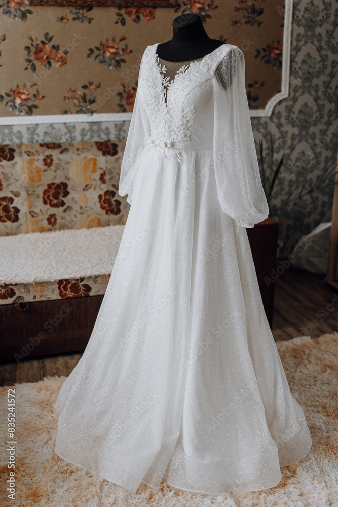 A long white dress with a floral pattern is displayed in a room. The dress is made of shiny material and has a long train A long white dress with a floral pattern is displayed in a room. The dress is made of shiny material and has a long train