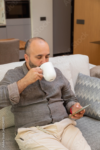 Man on the sofa with cup and smartphone in his hands photo