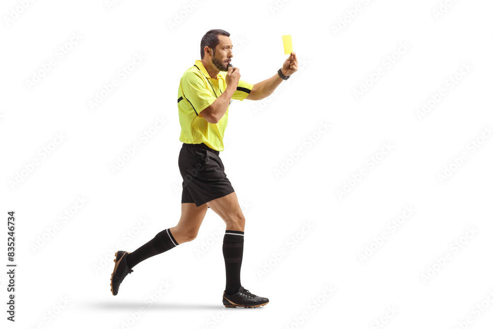 Full length profile shot of a football referee running and showing a yellow card