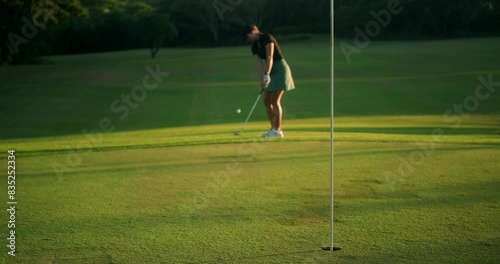 Young woman at a country club taking a golf lesson. A beginner golfer takes a swing and hits the ball, but misses the hole. She is upset but does not lose her positive attitude and smiles.
