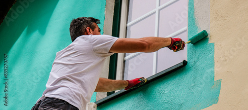 A worker paints the facade walls of a house with paint using a paint roller
