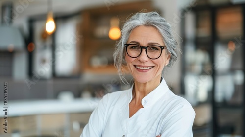 Portrait of a smiling older female doctor with glasses in a cozy, well-lit office. Ideal for concepts of healthcare, senior professionals, and medical expertise.