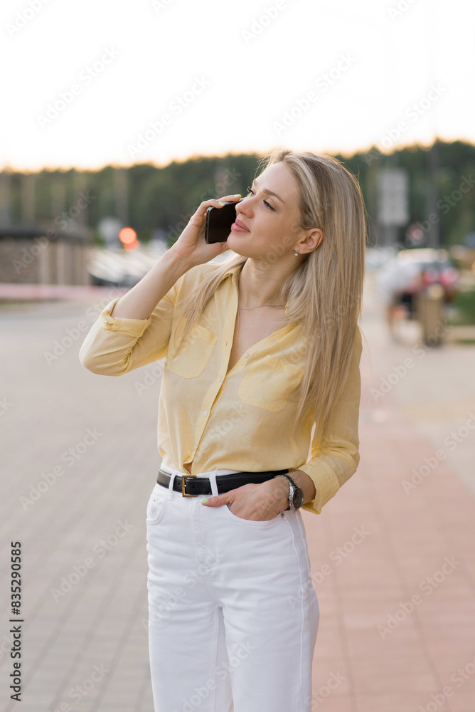 Young woman in casual clothes, talking on a cell phone, walking on a city street in the summertime