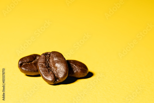 Three coffee beans close up isolated on a bright yellow surface background