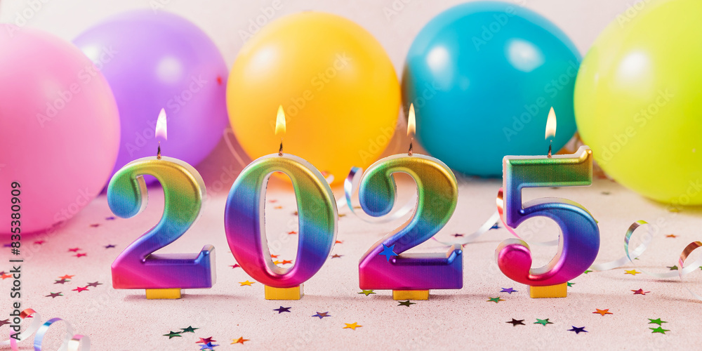 Holiday sparkling background banner Happy New Year 2025. Rainbow colored candles with numbers of year 2025 on background of colorful balloons and stars. New Year greeting card. Top view, flat lay