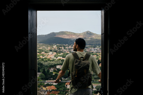 Travel and adventure concept. A young man with a retro-style green backpack stays in old town Bar in Montenegro country. Rear view. Looking at Houses with tiled roofs.