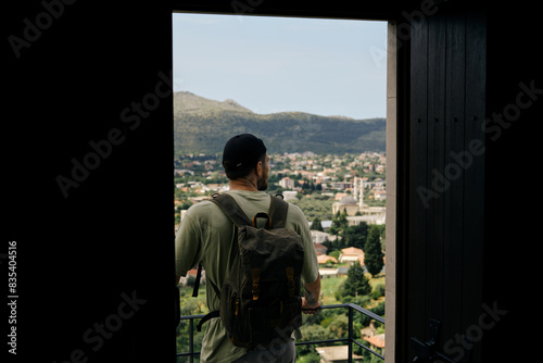 Travel and adventure concept. A young man with a retro-style green backpack stays in old town Bar in Montenegro country. Rear view. Looking at Houses with tiled roofs.