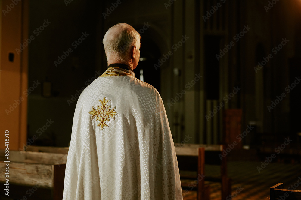 Naklejka premium Rear view of unrecognizable elderly Catholic priest wearing vestment standing in empty church, copy space