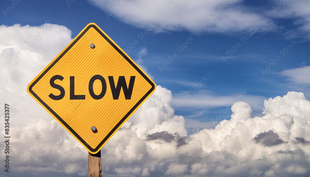 Yellow traffic sign with text SLOW with blue sky and white clouds on backdrop. Yellow traffic sign with text SLOW with blue sky and white clouds on backdrop.