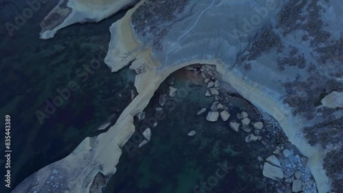 Tat-Tonn or Spritzing rock, snorkeling point between Qarraba Bay and Ta'Babu Cove, Ghajn Tuffieha, Mgar, Malta. Aerial view of the emerald sea and rocky coast in early morning still in the shade of photo