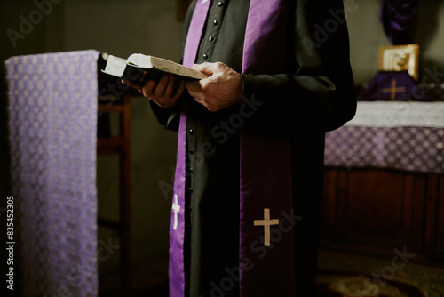 Crop shot of unrecognizable senior Catholic priest wearing soutane and stole standing indoors reading Bible