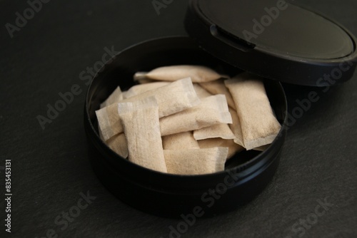 An open box of nicotine pouches. Nicotine pads in black packaging on a dark surface. 